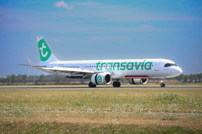 A white Transavia passenger jet taxiing on an airport runway near green fields